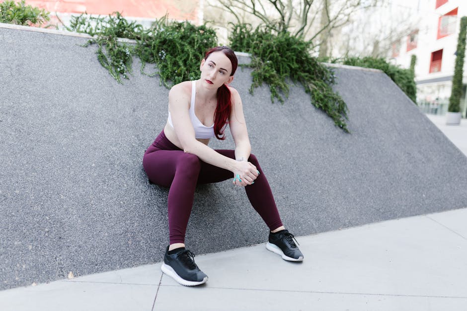 A woman in stylish activewear sits outdoors on a modern concrete bench with green plants.