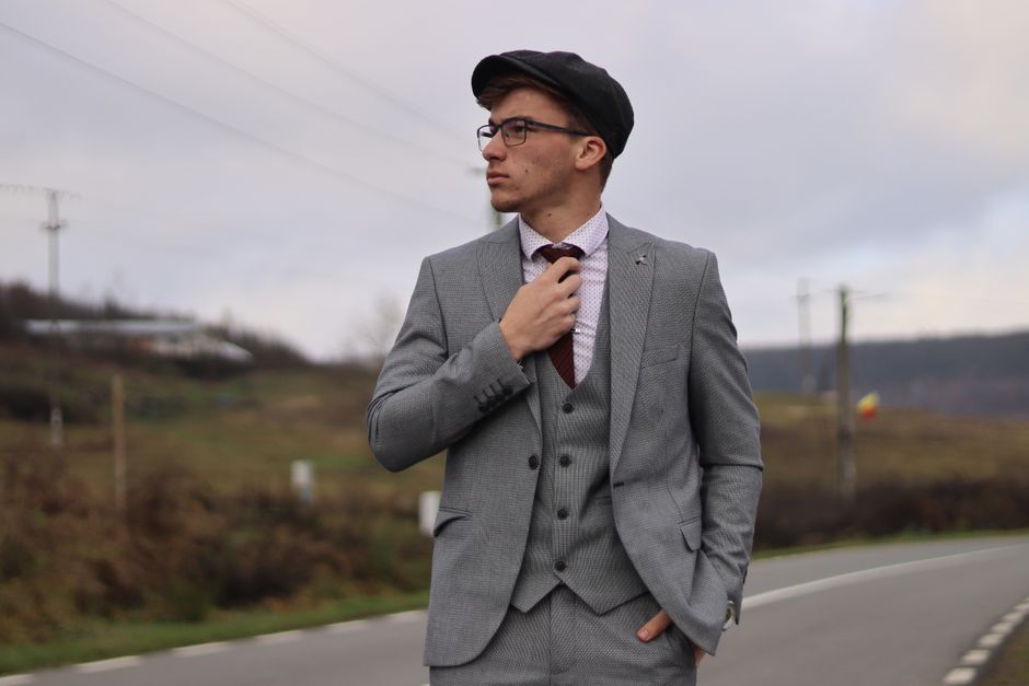 A fashionable man in a grey suit confidently poses on a rural road, exuding elegance and poise.