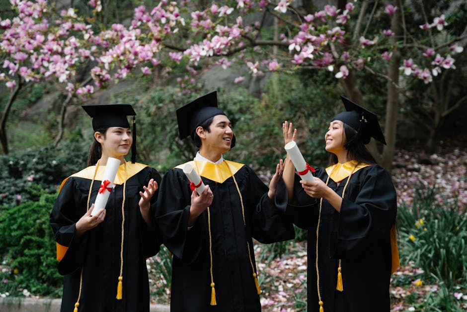 Three young graduates in caps and gowns celebrate with diplomas under blooming trees.