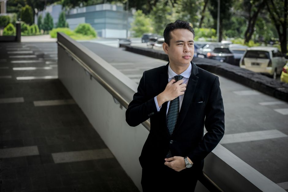 Confident young man in a suit adjusts his tie outdoors, exuding professionalism.