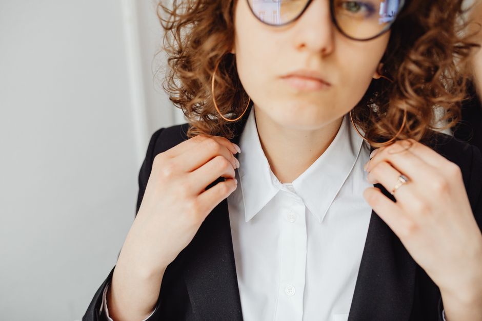 Close-up of a confident woman in a black blazer and white shirt adjusting collar.