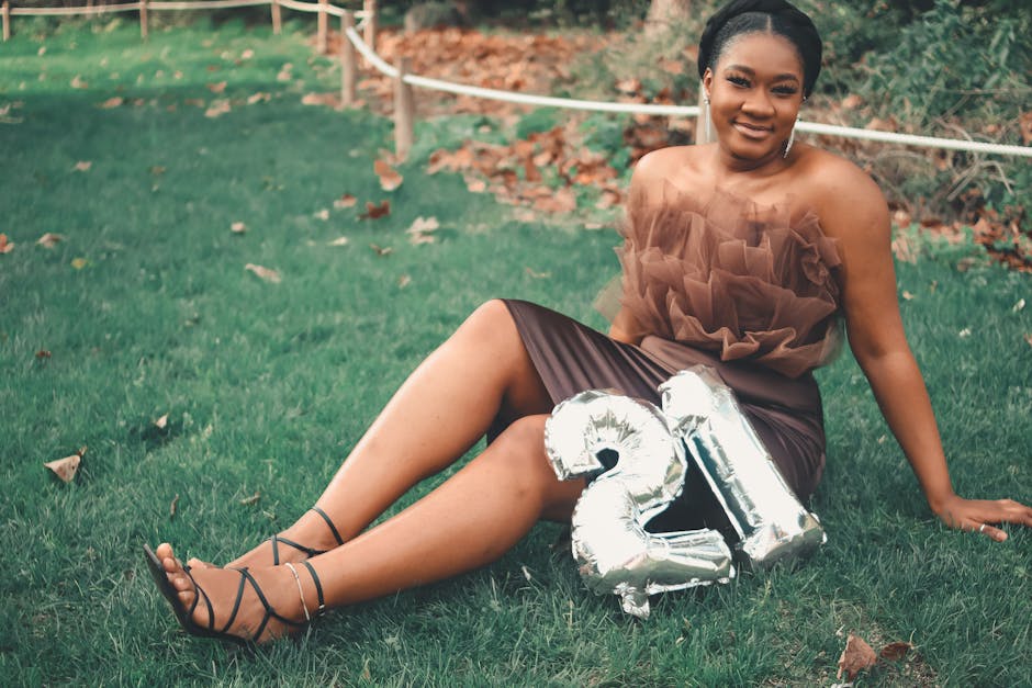 Happy young woman in a brown dress celebrating her 21st birthday outdoors with balloons and a smile.