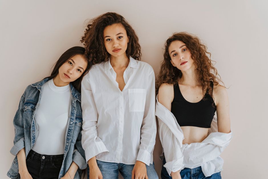 Three stylish, diverse women in casual attire stand confidently against a neutral background.