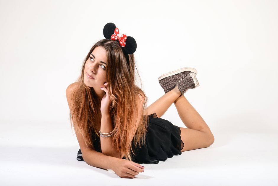 Young woman wearing a mouse ears headband, relaxing indoors against a white background.
