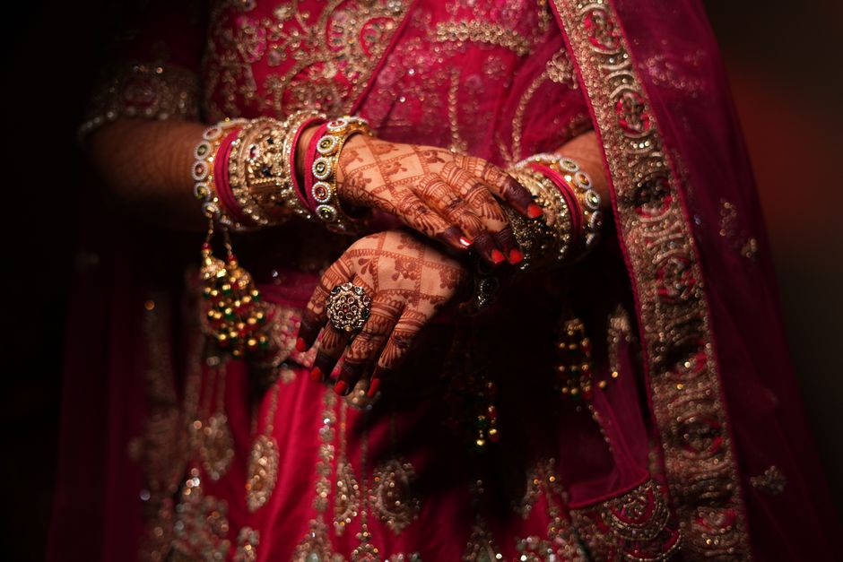 Close-up of Indian bride's hands adorned with mehndi and traditional jewelry, showcasing rich cultural heritage.